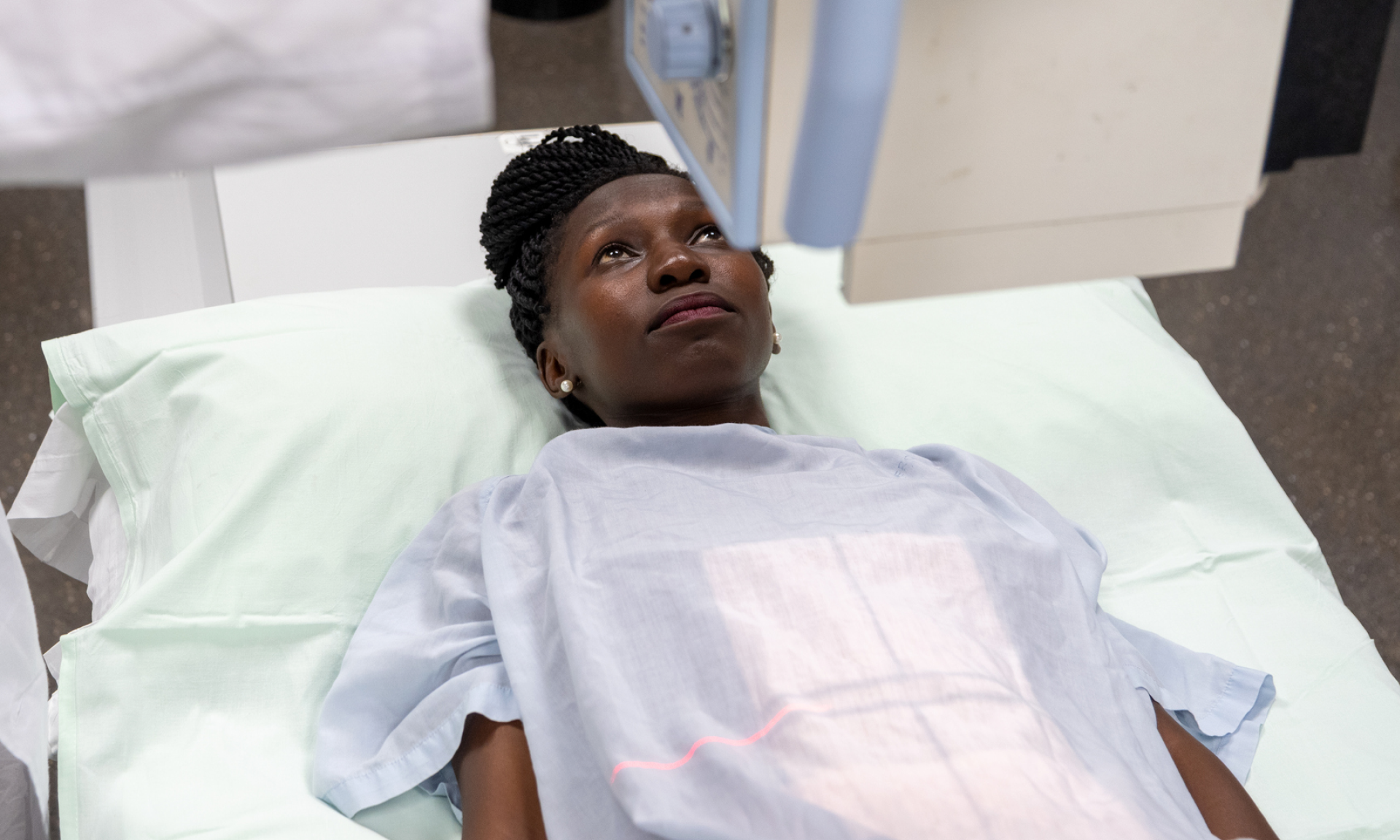 A Black woman lying on a hospital bed under an x-ray machine